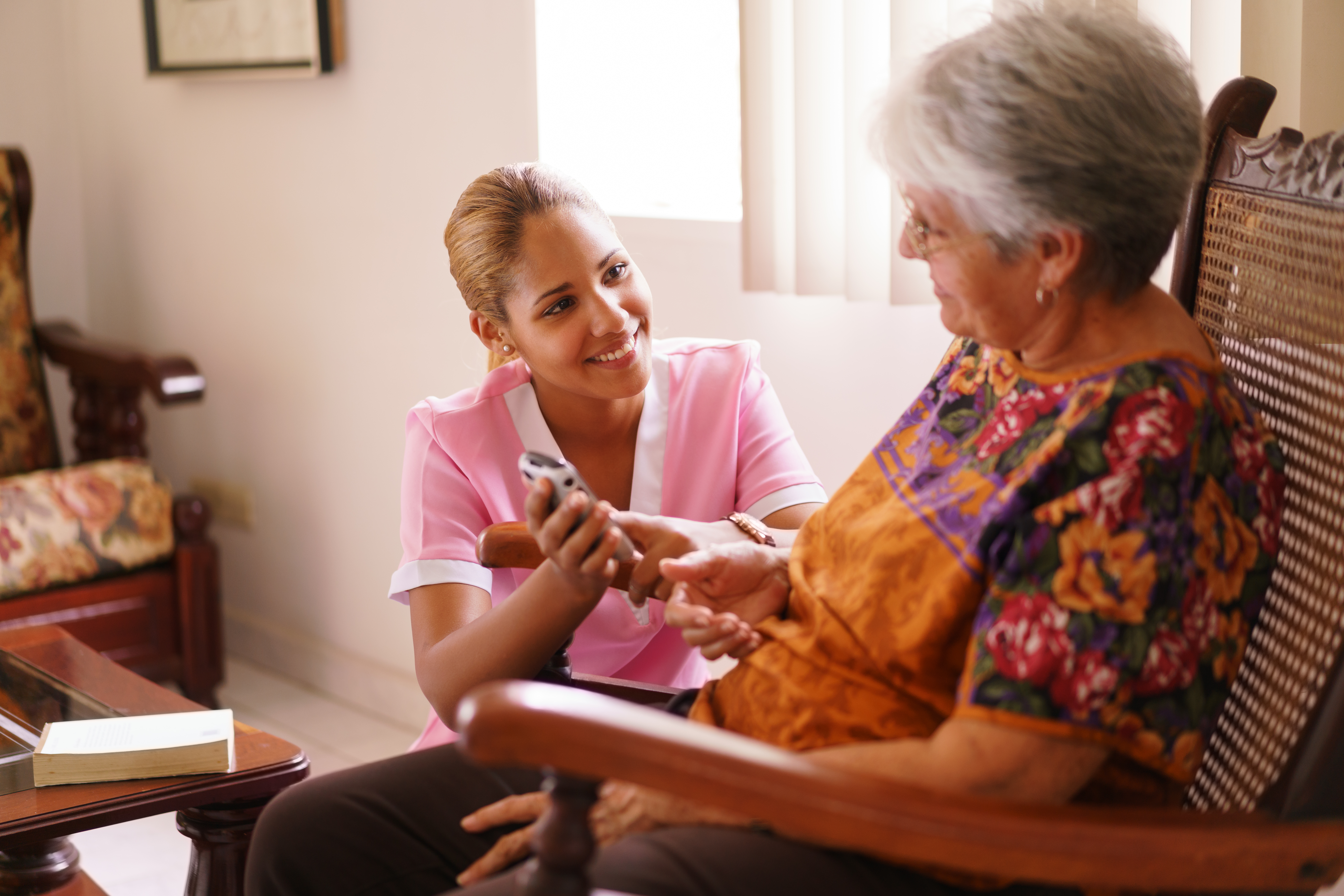 Old people in geriatric hospice: elderly lady having eyesight problems viewing the screen of mobile phone. A nurse helps the senior woman dialing a number on the tiny keyboard